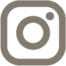 Instagram logo in a simple, minimalist design, featuring a circular camera icon and a square outline, presented in a muted brown color.